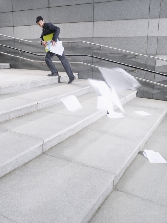 Business man walking up steps losing papers from briefcase outdoors side viewの写真素材