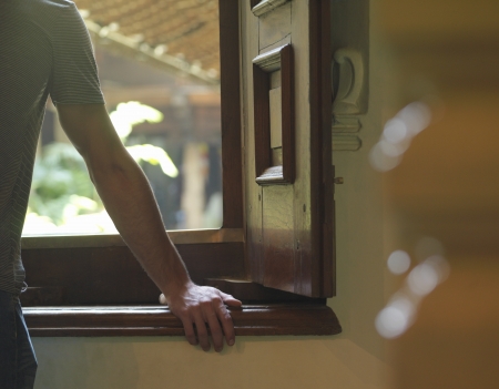 Young man looking trough window leaning on windowsill back view selective focusの写真素材