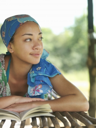 Portrait of young woman wearing kerchief lying with book in hut lying down smilingの写真素材