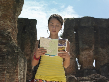 Young woman reading guide book ancient ruins in backgroundの写真素材