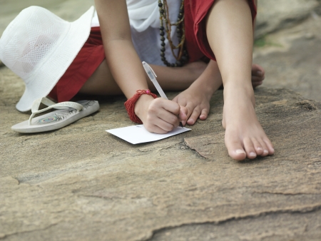 Young woman sitting on rock writing low sectionの写真素材