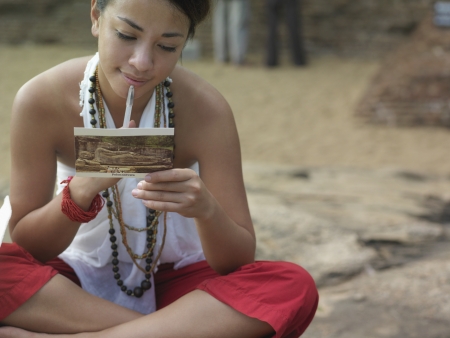 Young woman sitting on rock reading postcard mid sectionの写真素材