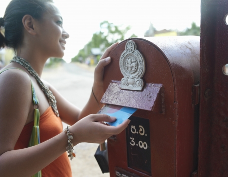 Young woman putting postcard to mailbox smilingの写真素材