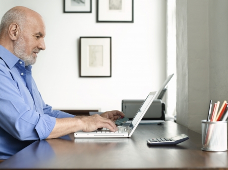 Middle-aged man sitting at desk using laptop profileの写真素材