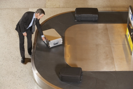 Business man claiming suitcase at luggage carousel in airportの写真素材