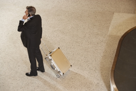 Business man using mobile phone by baggage claim in airportの写真素材