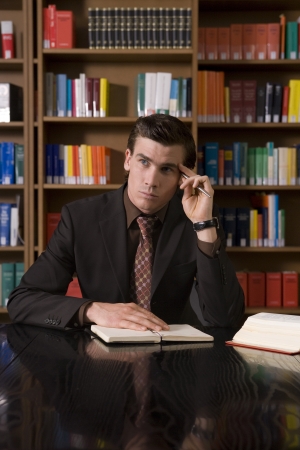 Pensive man wearing suit with book at desk in libraryの写真素材