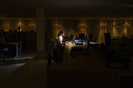 Woman working at laptop in dark officeの写真素材