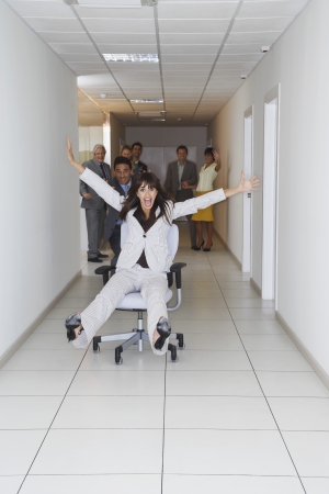 Office workers playing on office chairs in hallwayの写真素材