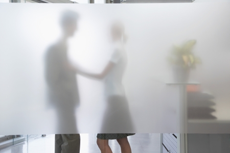 Female office worker touching male colleague behind translucent wall in officeの写真素材