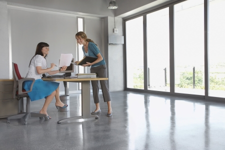 Two women discussing document at desk in empty office buildingの写真素材