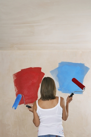 Woman facing wall painted on ble and red holding with paint rollers back viewの写真素材