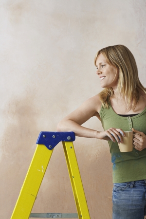 Smiling woman leaning on step ladder holding mugの写真素材