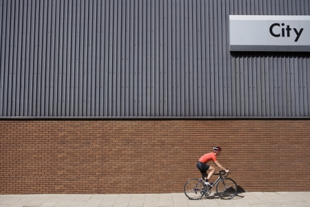 Man cycling past building with 'City' written on sideの写真素材