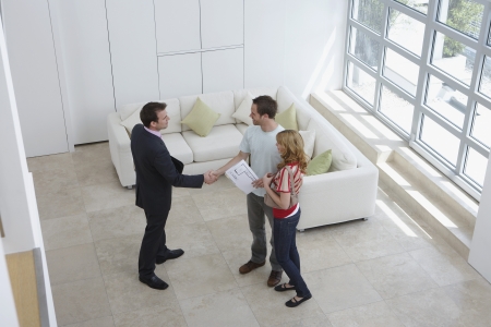 Real estate agent with couple in new home man shaking hand elevated viewの写真素材
