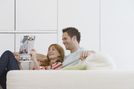 Couple reading brochure on sofaの写真素材