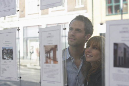 Couple looking through window at estate agentsの写真素材