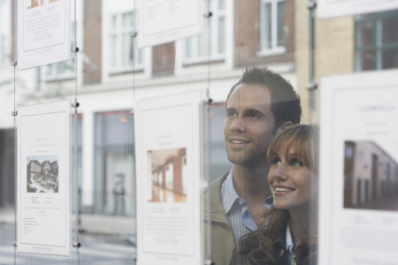 Couple looking through window at estate agentsの写真素材
