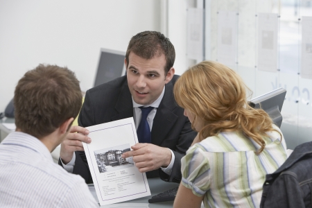 Couple observing brochure with real estate agent in officeの写真素材