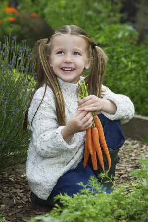 Girl (5-6) holding carrots in gardenの写真素材