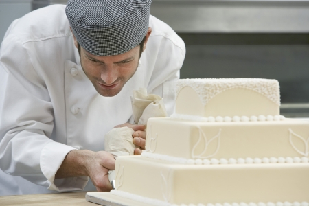 Male chef icing wedding cake in kitchenの写真素材
