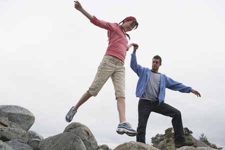 Couple holding hands jumping on rocksの写真素材