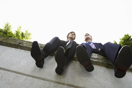 Two business men sitting side by side on wall low angle viewの写真素材