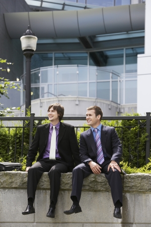 Two business men sitting on wall outside officeの写真素材