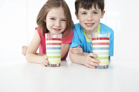 Boy and girl (5-6) sitting at table holding colourful glasses portraitの写真素材