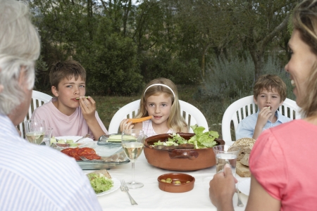 Three-generation family with three children (6-11) sitting at table in gardenの写真素材