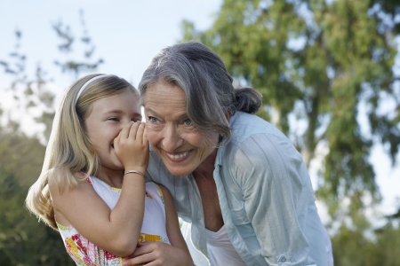 Young blonde girl whispering in grandmother's earの写真素材