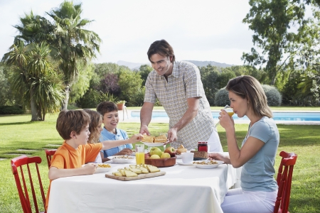 Family with three children (6-11) sitting at breakfast table outdoorsの写真素材