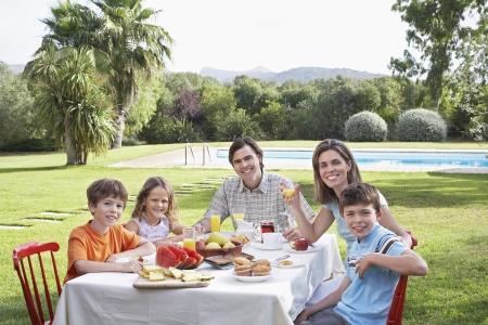 Family with three children (6-11) sitting at table in garden portraitの写真素材