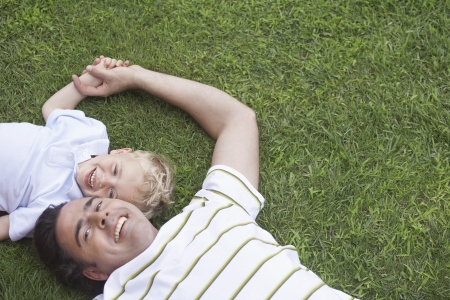 Father and young son (3-4) lying on grass portraitの写真素材