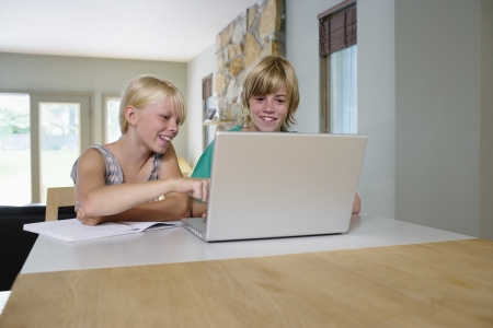 Sister and brother (8-11) sitting at table using laptop smilingの写真素材
