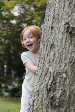 Portrait of girl (3-4) peeking from behind tree laughingの写真素材
