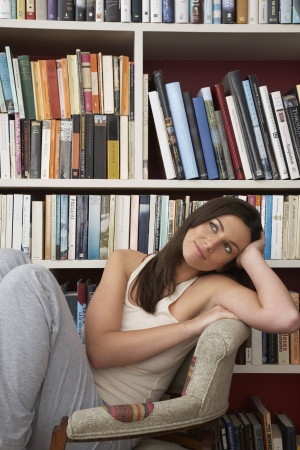 Young woman relaxing in chair by bookshelfの写真素材