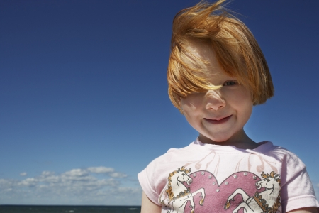 Portrait of ginger haired girl (5-6) against blue skyの写真素材