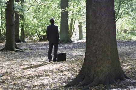 Business man standing with briefcase in middle of forestの写真素材