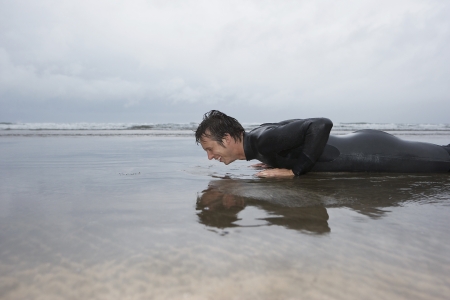 Man in wetsuit doing pushups in shallow water on beach side viewの写真素材