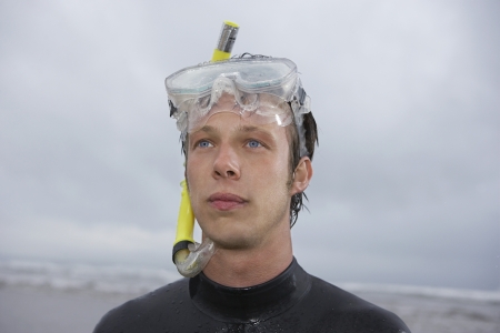 Man in wetsuit wearing snorkle standing on beach portraitの写真素材