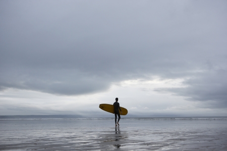 Surfer carrying surfboard on beach back viewの写真素材