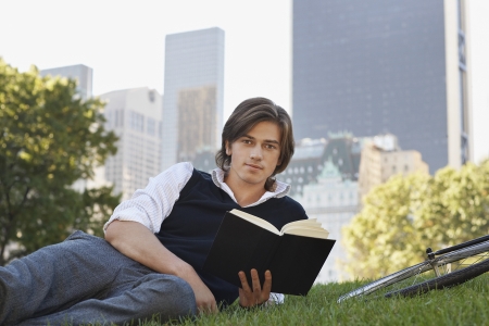 Man lying on lawn holding book portraitの写真素材