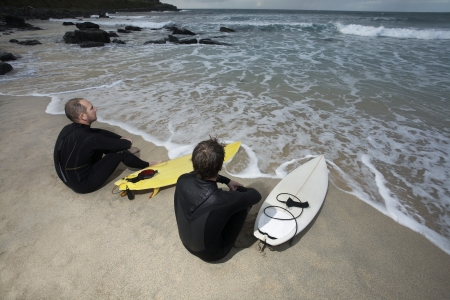 Two surfers sitting on beach looking at sea elevated viewの写真素材