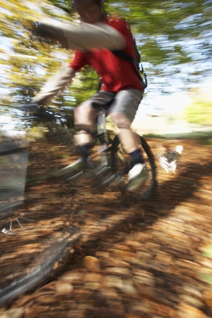 Dog chasing person on mountain bike through woodland motion blurの写真素材