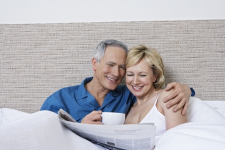 Middle aged couple in bed woman reading newspaper man drinking coffeeの写真素材