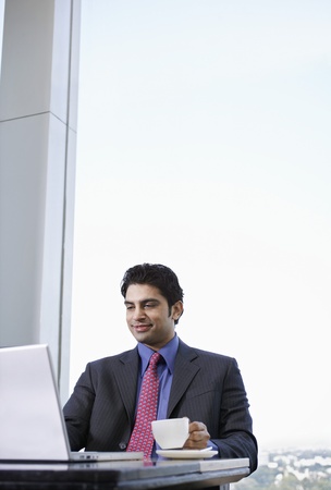 Business man using laptop holding tea cupの写真素材
