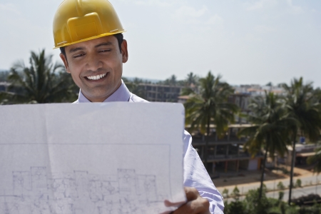 Architect wearing a yellow hard hat looking at blue prints at construction siteの写真素材