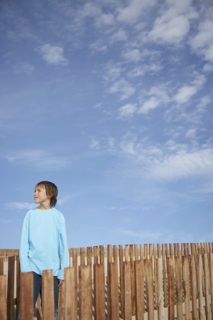 Boy (10-12) standing between wooden fences on sand duneの写真素材