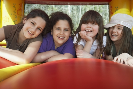 Four girls (7-12) lying in row in bouncy castle laughing portraitの写真素材
